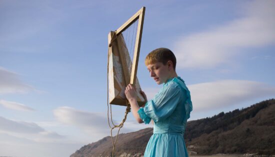 Photo d'une femme manipulant une sorte de harpe D.I.Y avec la mer, le ciel et une île en arrière plan